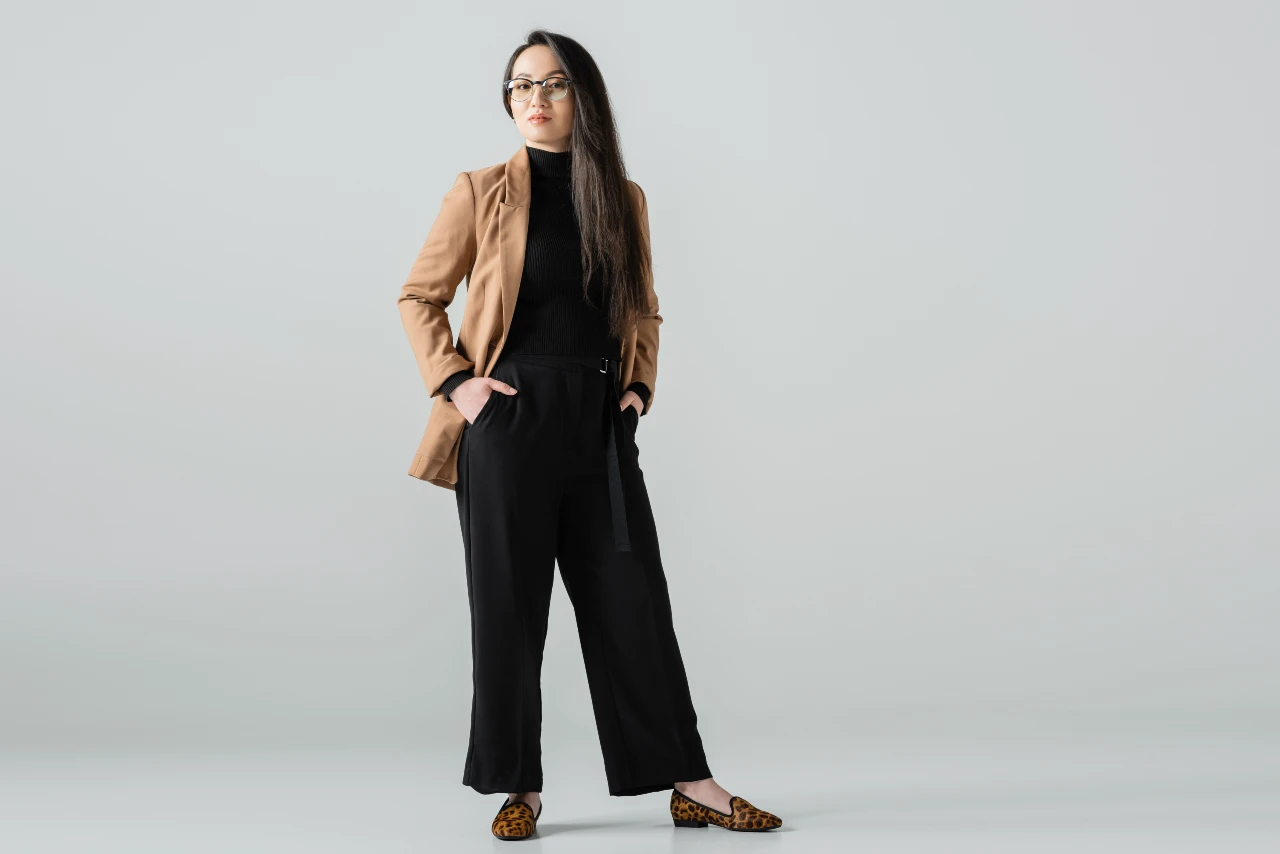 Business Casual Look modern gedacht: Blazer zu Rollkragen und weit geschnittener Stoffhose. Frau trägt Blazer in Cognac-Farbe zu schwarzem Rollkragenpulli, schwarzer Stoffhose und Ballerinas mit Leoprint – moderner Business Look