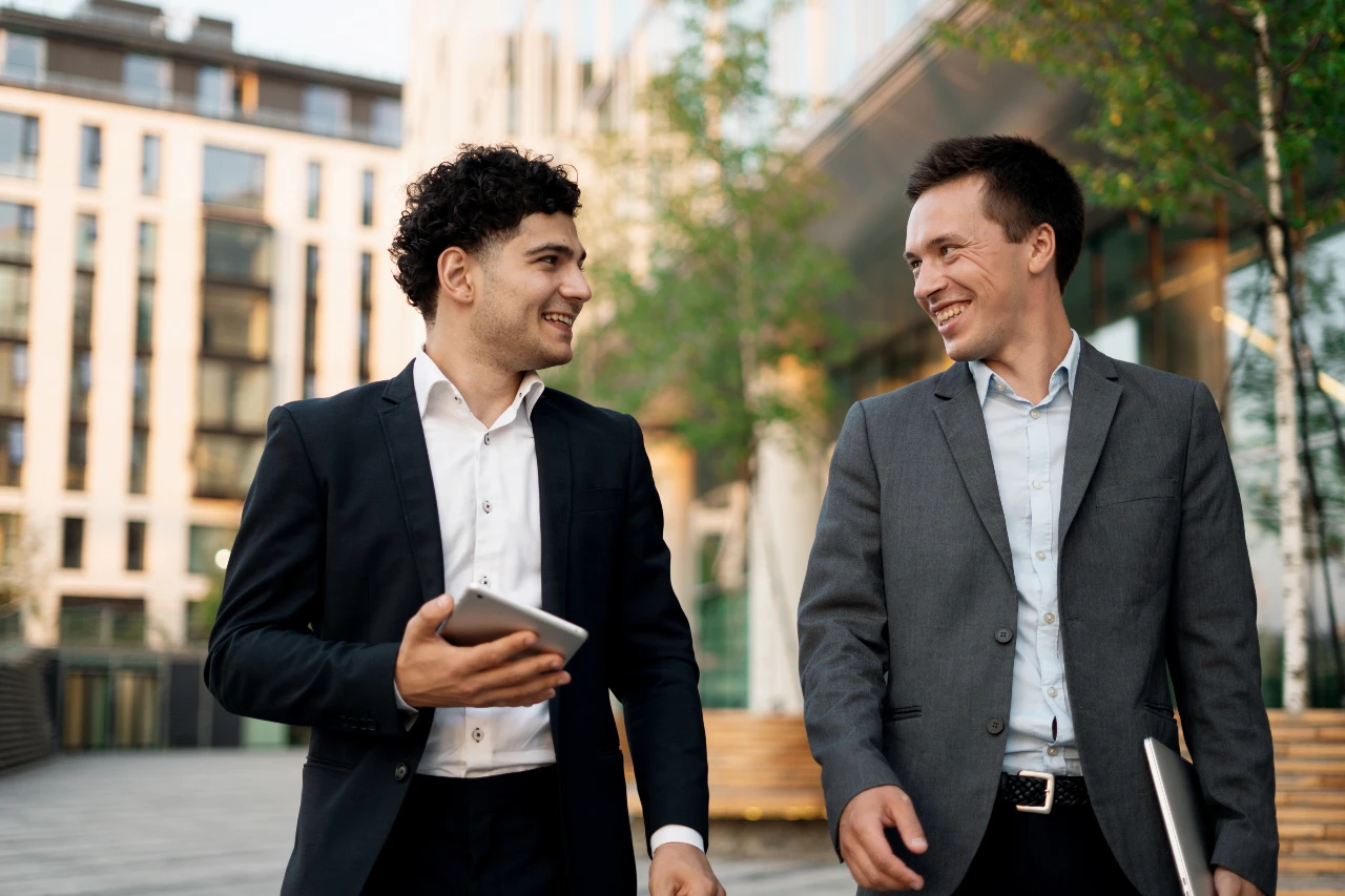 Keine Krawatte nötig! Der Business Casual Look kombiniert Sakko und Anzughose mit klassischem Hemd. Männer laufen nebeneinander, tragen Sakko, Anzughose und Hemd, ohne Krawatte.