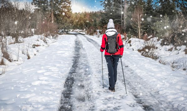 Wandern bei Schnee ist mit der richtigen Kleidung kein Problem Wanderin folgt einer Reifenspur im Schnee