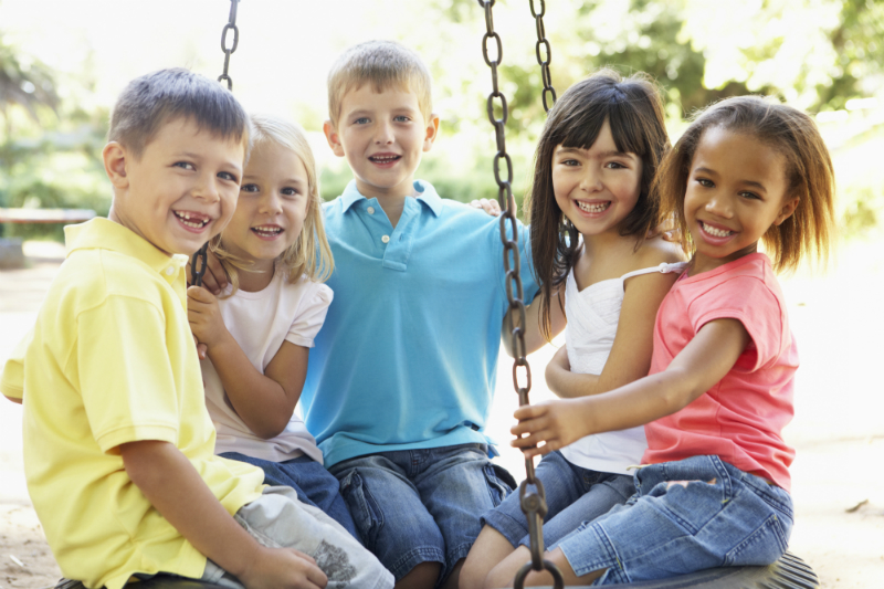 Sommerlich gekleidete Kinder sitzen in einer Nestschaukel