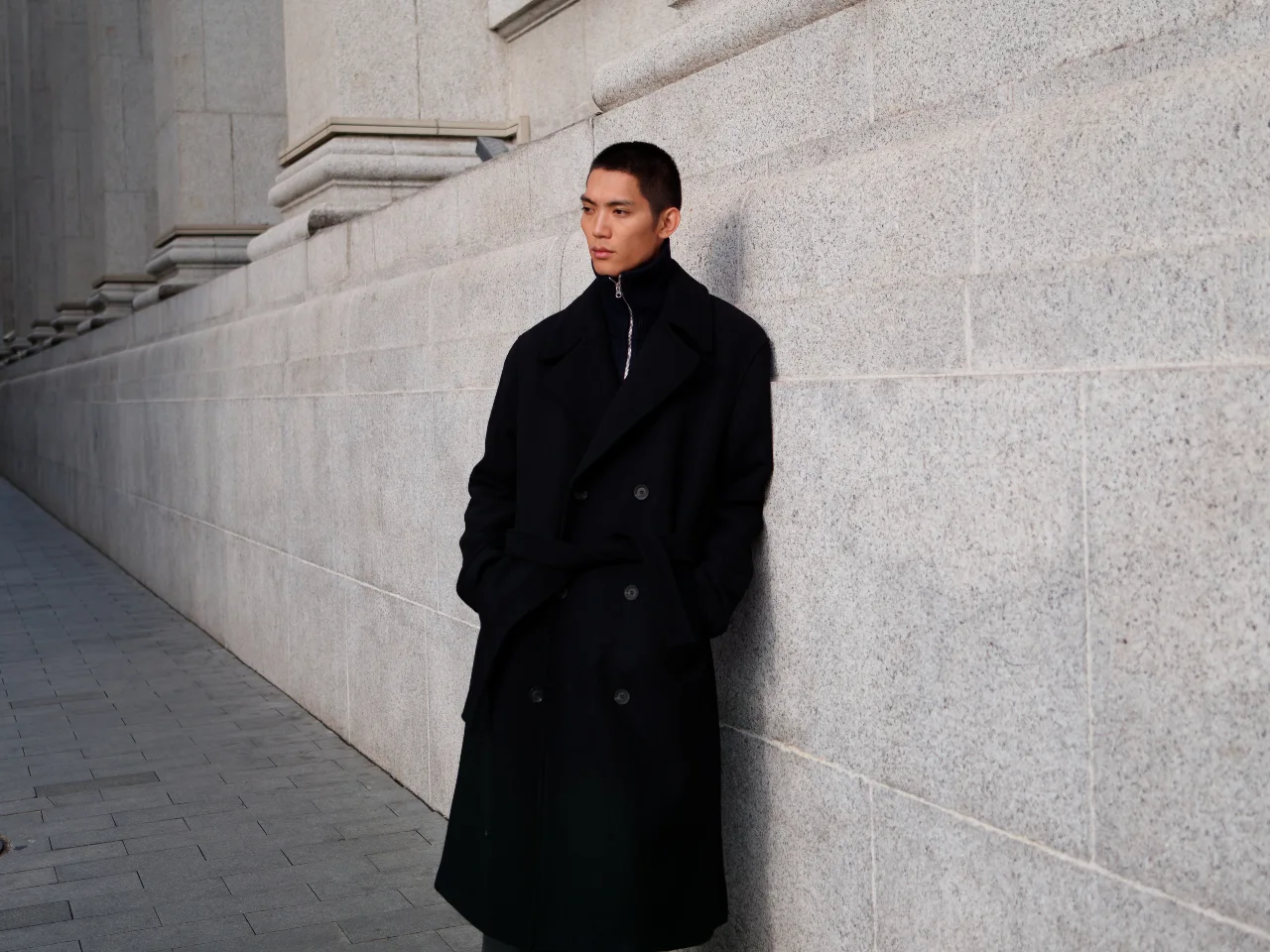 Mann trägt den Casual Chic Look in all black, schwarzer Mantel, trifft auf schwarzen Seefahrer-Pulli und schwarze Hose