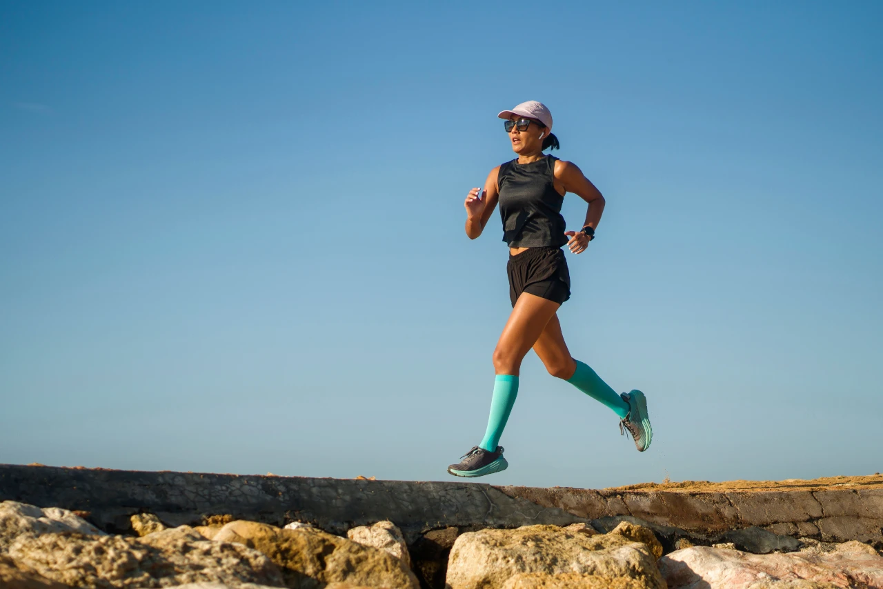 Frau läuft mit sommerlicher, atmungsaktiver Laufbekleidung – kurze Laufshorts, Cap und Kompressionssocken