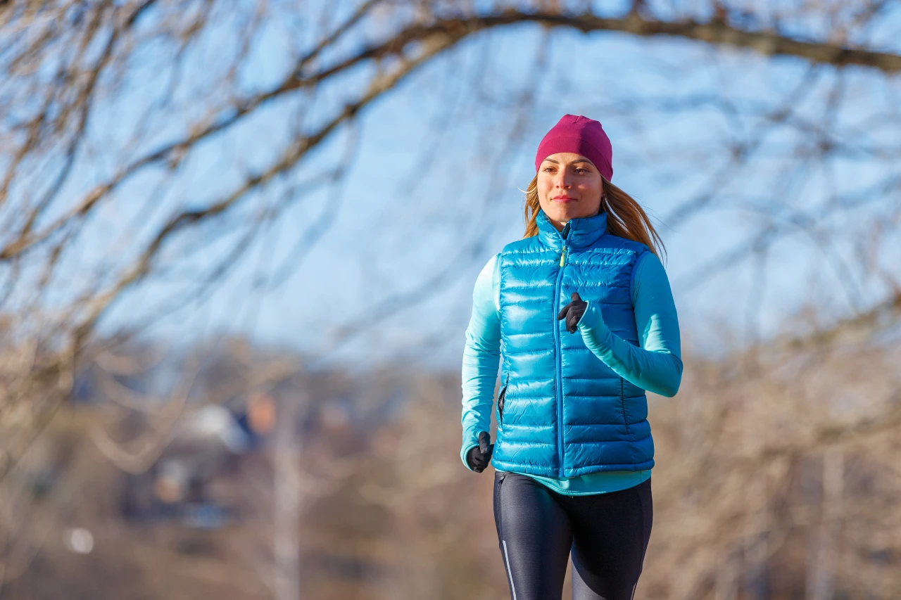 Frau joggt im Winter und trägt als Laufbekleidung Daunenweste und Longsleeve