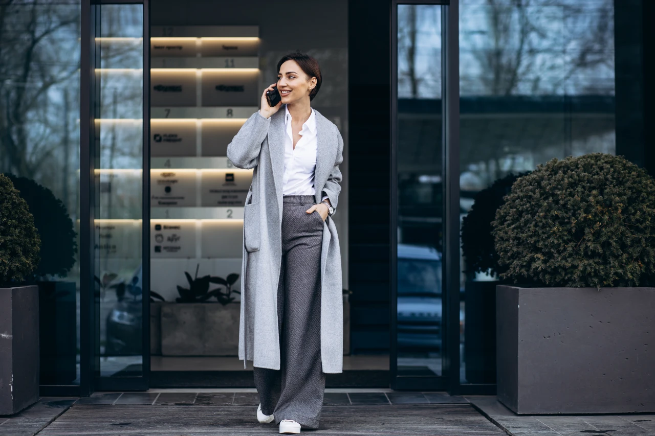 Frau trägt einen eleganten hellgrauen Wollmantel zu einer weiten Stoffhose und Bluse.