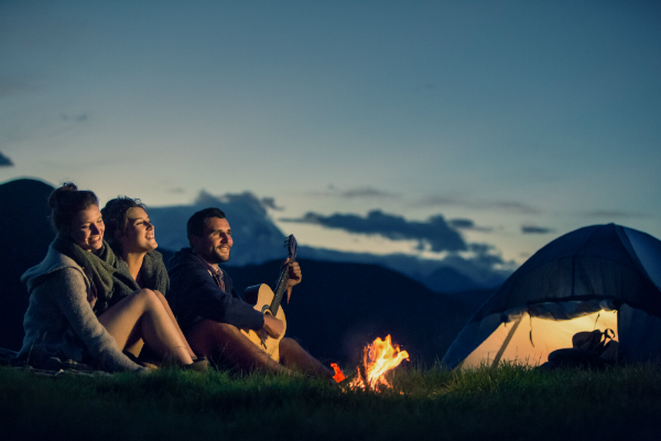 Drei Freunde campen mit einer Gitarre vor dem Lagerfeuer