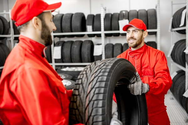 Zwei Maenner in roter Uniform arbeiten im Lager mit Autoreifen