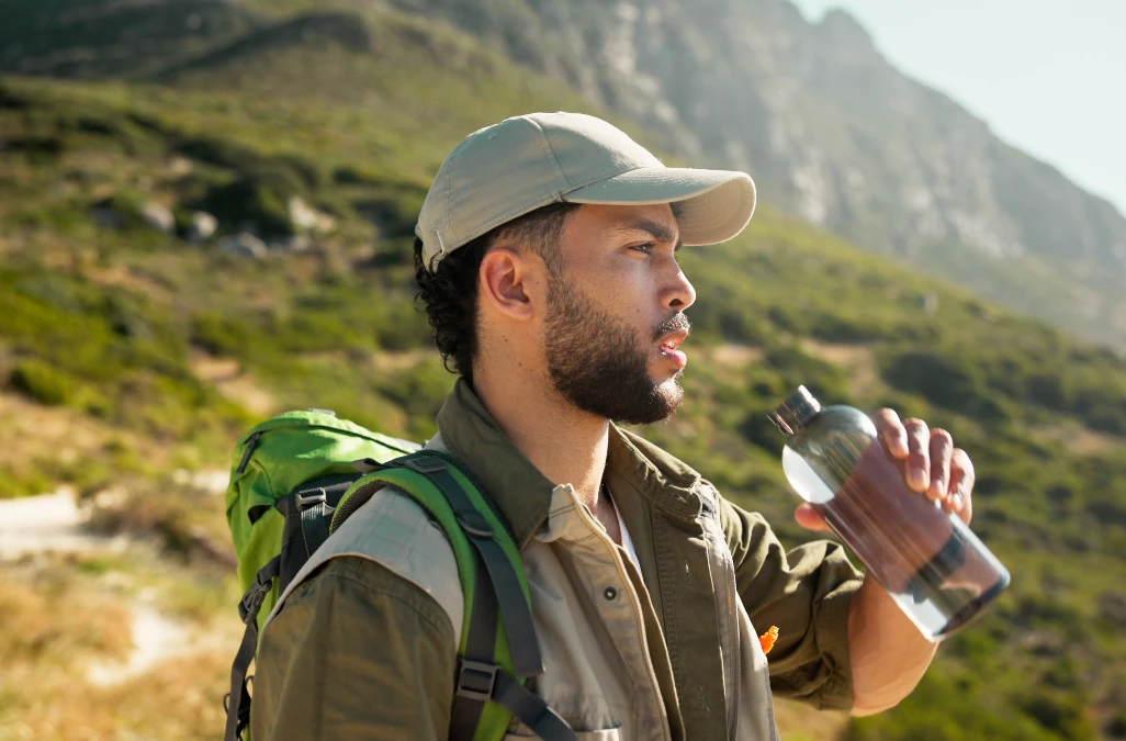Eine Cap sollte leicht sein und vor UV-Strahlung schützen. Mann trägt eine Cap zum Wandern und trinkt aus einer Flasche