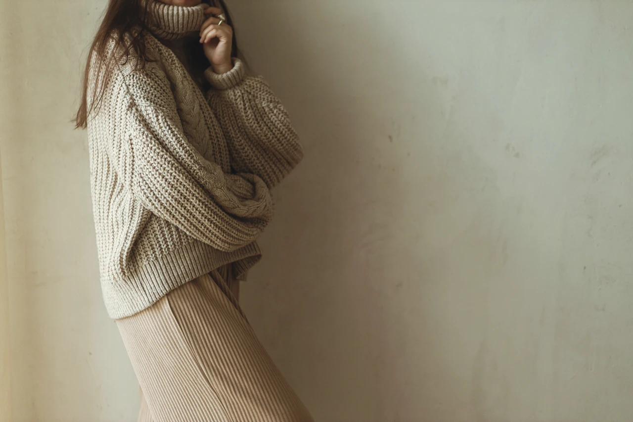"Minimal chic" mit Strickpullover Frau mit braunem Haar trägt grob gestrickten Pullover in Beige.