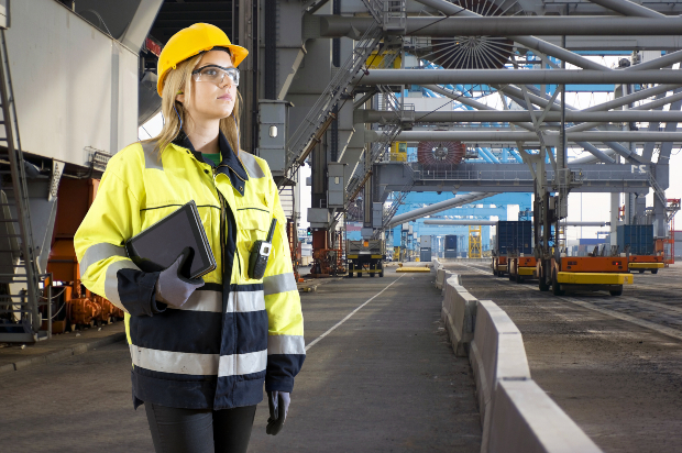 Frau in Sicherheitsjacke, mit Helm und Handschuhen und Sicherheitsbrille