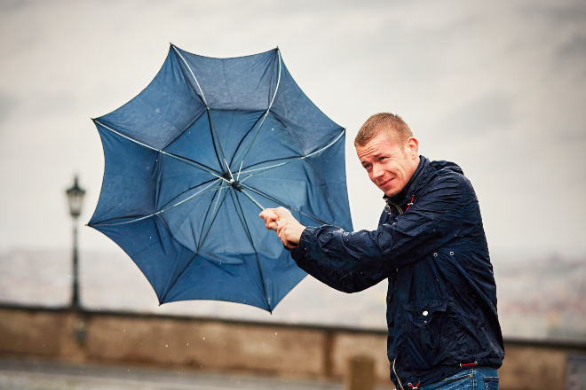 Mann mit Regenschirm im Wind - Ideale Schlechtwetterkleidung sieht anders aus