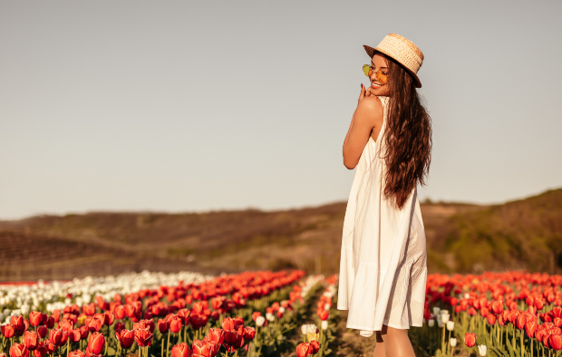 Junge Frau in weißem leichten Kleid steht im Blumenfeld - Sommertrends der Mode 2020