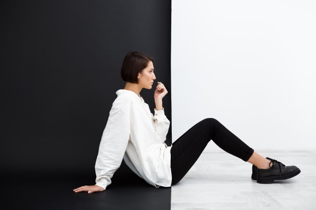Eine Frau, gekleidet mit einem weißen Hemd und einer schwarzen Hose, sitzt vor einer kontrastierenden Wand. Kontrastfarben liegen im Trend 