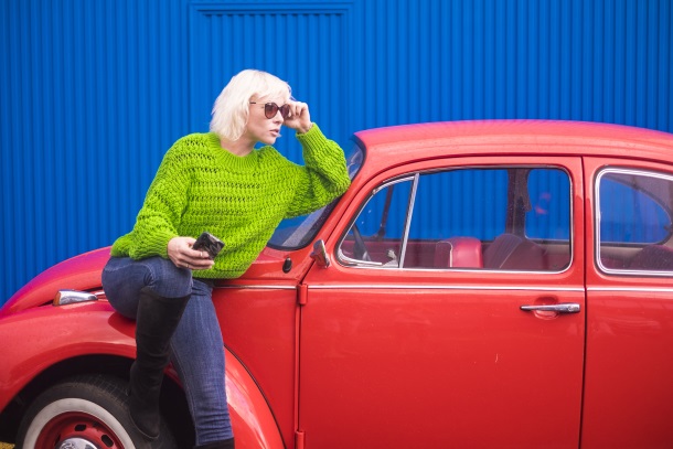 Eine Frau in blauen Jeans und einem grünen Pullover sitzt auf einem roten VW-Käfer Kleidungsfarben: Grell oder dezent 