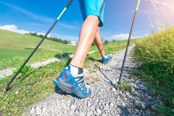 Blick auf die Beine eines Mannes, der Nordic-Walking betreibt. Er läuft an einem sonnigen Tag auf einem Feldweg im Walking Outfit