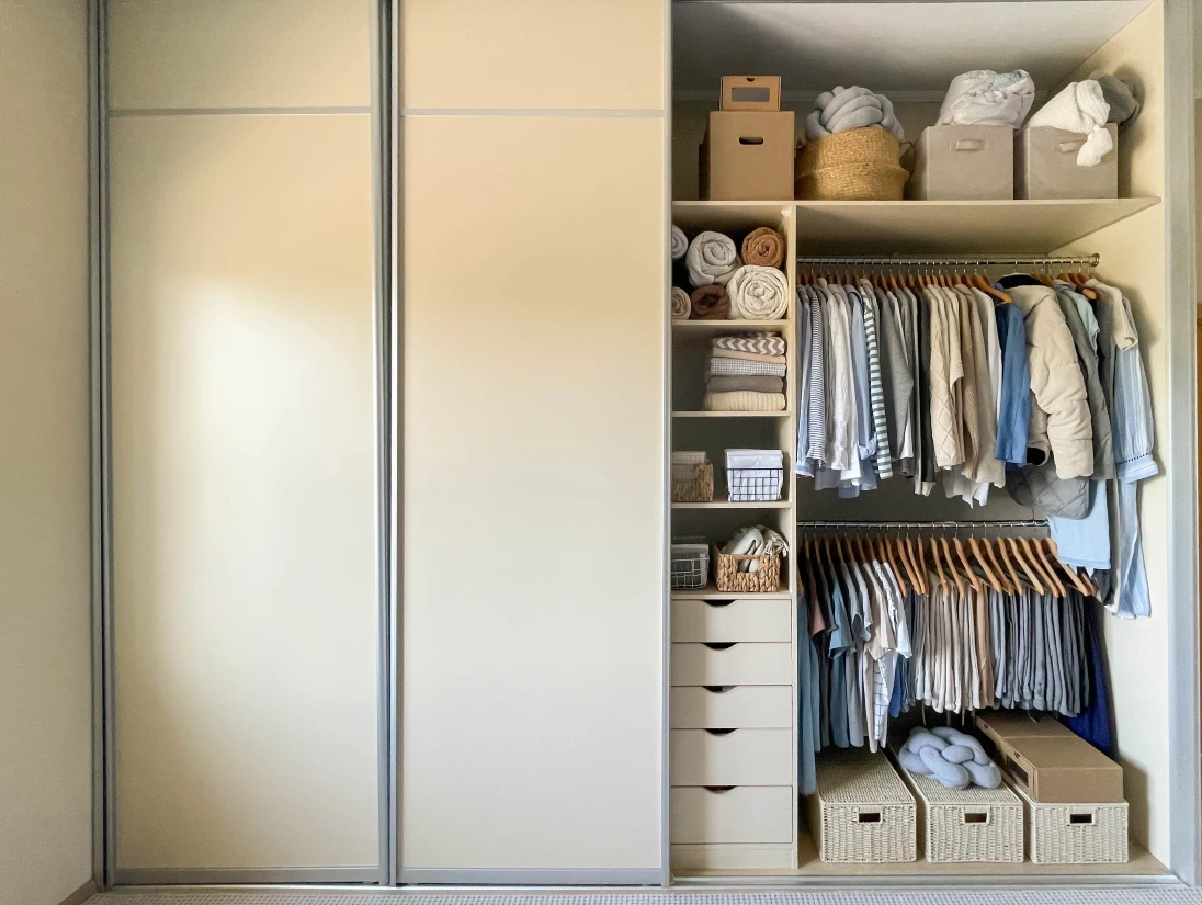 Ein Kleiderschrank ist von einer Seite geöffnet, innen hängt die Kleidung sortiert nach Kategorien