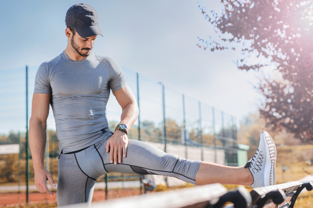 Ein sportlicher Mann in Running-Wear dehnt sein Bein an einer Parkbank