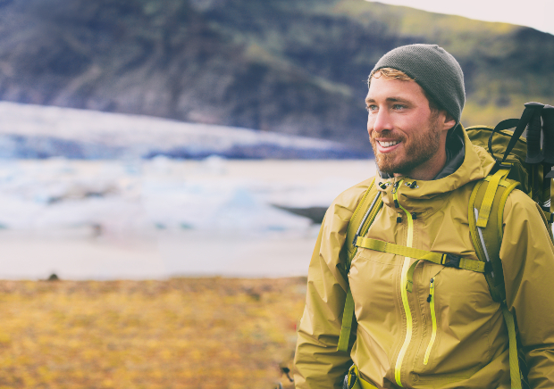 Ein junger Mann mit Rucksack, Outdoorjacke und Mütze wandert bestens gerüstet einen Berg hinauf 