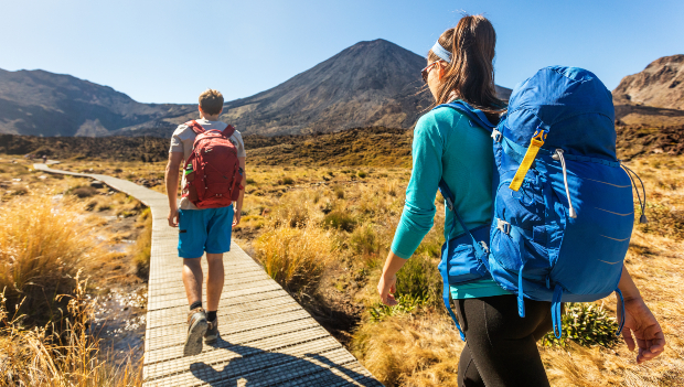 Ein junger Mann und eine junge Frau wandern über einen Steg auf einen Berg in der Ferne zu