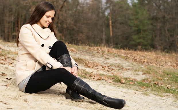 Eine Frau mit Leggings und Boots sitzt auf einer sandigen Lichtung im Wald