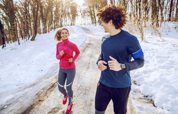 Eine junge Frau und ein junger Mann joggen durch eine verschneite Landschaft