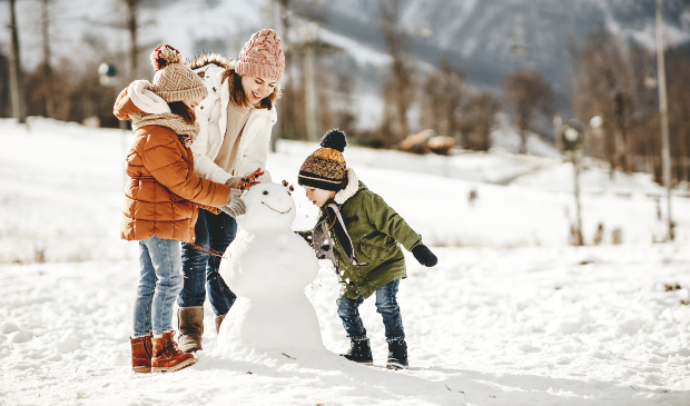 Mutter mit Kindern baut Schneemann während einer Winterwanderung