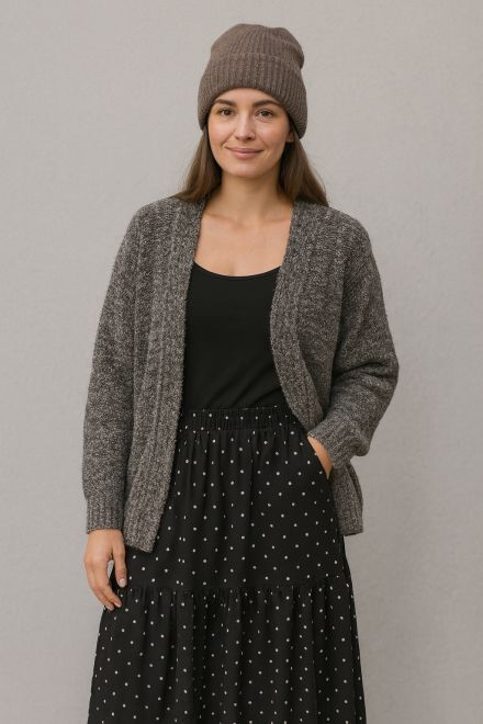 Frau im Winteroutfit mit grauer Strickjacke, schwarzem Spaghettiträger-Top, gepunktetem Maxirock und Strickmütze