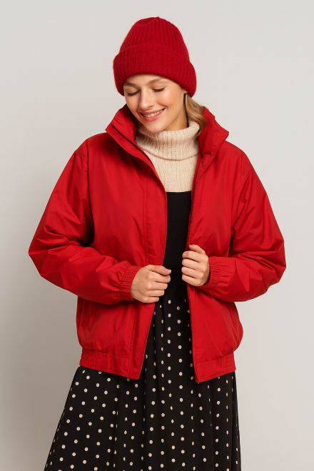 Frau im Winteroutfit mit roter Jacke, passender Mütze, Rollkragenpullover und gepunktetem Rock