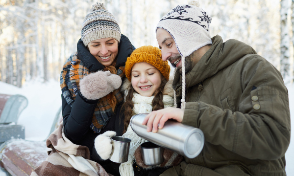 Mutter, Vater und Tochter rasten auf einer Winterwanderung und gönnen sich ein Becher heißen Tee