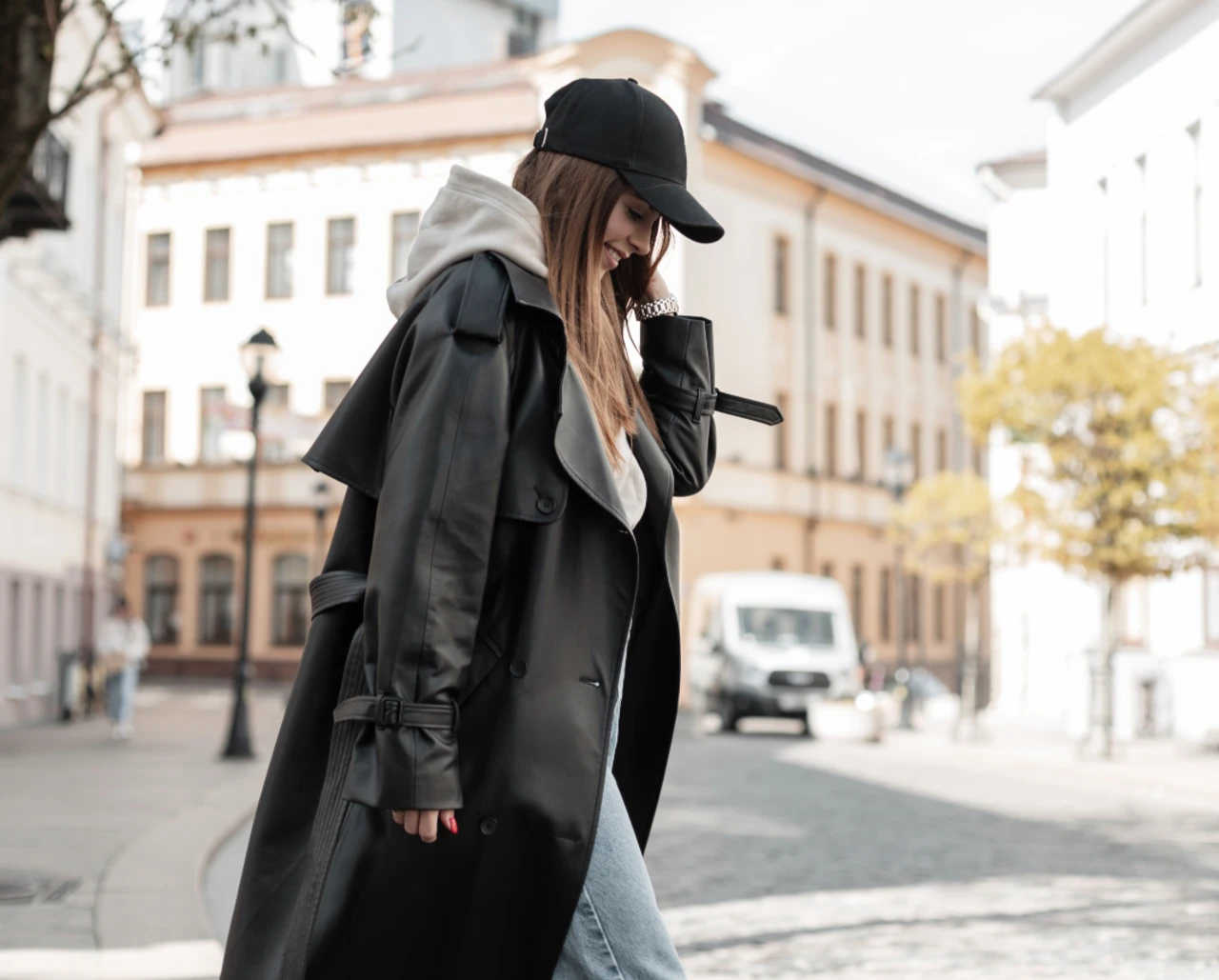Frau trägt einen langen schwarzen Mantel, grauen Hoodie und schwarze Cap als klassischen Berlin Style