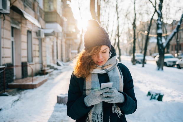 Junge Frau im Winter benutzt Handy mit Handschuhen