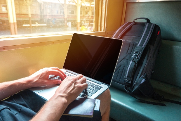 Junger Mann reist mit Laptop und Tasche im Zug - Laptop-Rucksäcke für die Reise