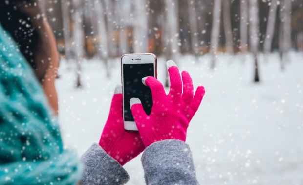 Junge Frau mit Handy und Touchscreen-Handschuhen