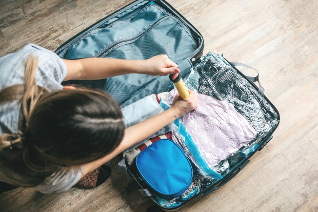 Das Vakuumieren entzieht Luft und sorgt somit für mehr Platz Junge Frau vakuumiert Kleidung im Reisekoffer