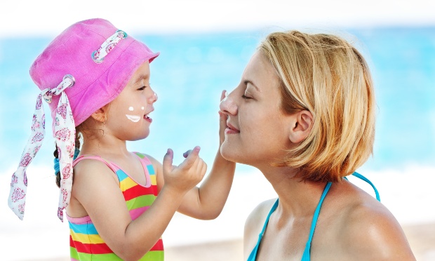 Kleines Mädchen schmiert der Mutter Sonnencreme ins Gesicht - Verreisen mit Kind