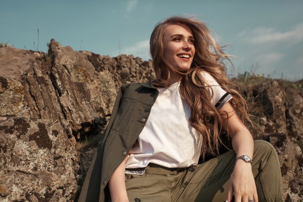 Eine junge Frau posiert im Sommer vor einem Felsen. Um ihre Schultern liegt eine Baumwolljacke