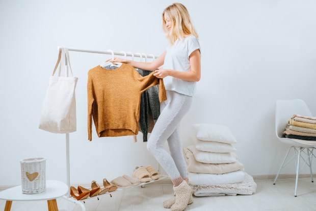 Eine junge Frau nimmt einen Pullover von der Kleiderstange in ihrem Ankleidezimmer Grundausstattung im Kleiderschrank
