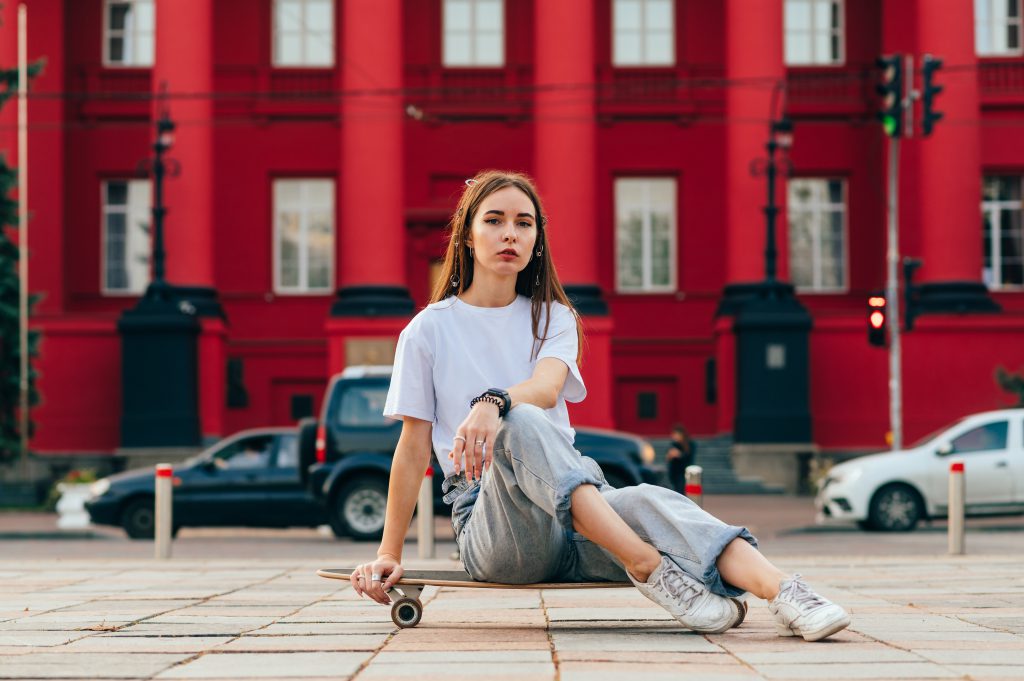 Junge Frau in Baggy Jeans sitzt auf Skateboard