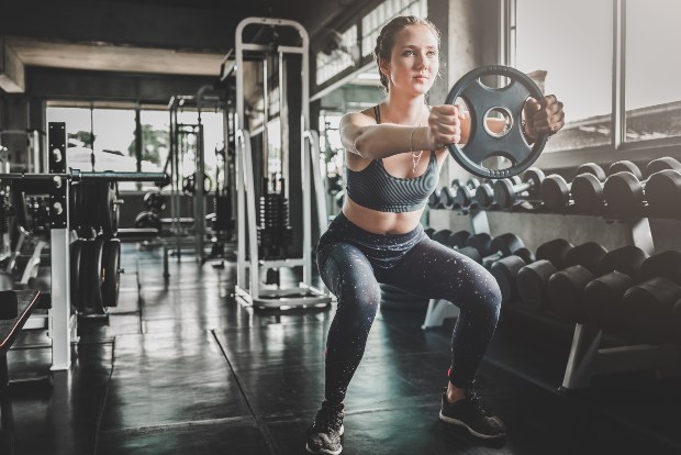 Ein junge Frau trainiert mit Gewischten im Fitnessstudio