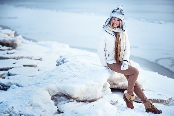 Eine Frau mit Schnürboots sitzt vor einer winterlich verschneiten Landschaft Winteroutfits für Damen
