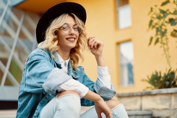 Eine junge Frau, die Jeanshose und Jeansjacke trägt, lächelt in die Kamera Modetrends 2023