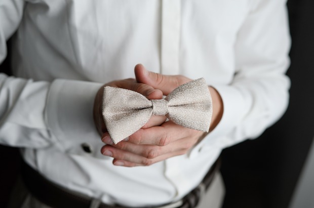 Mann mit weißem Hemd hält eine weiße Fliege in den Händen - "White Tie" Dresscode Hochzeit 