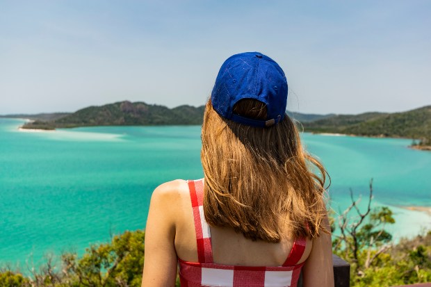 Junge Frau blickt aufs Meer, sie trägt u.a. eine blaue Basketball Kappe