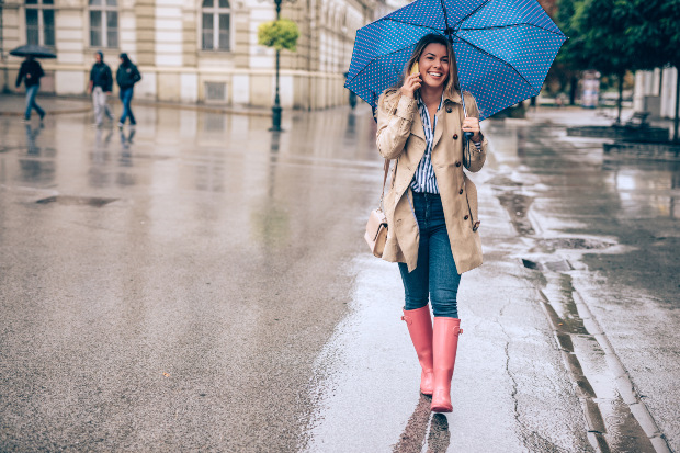 Eine Frau in pinkfarbenen Gummistiefeln spaziert mit einem Regenschirm durch die Stadt