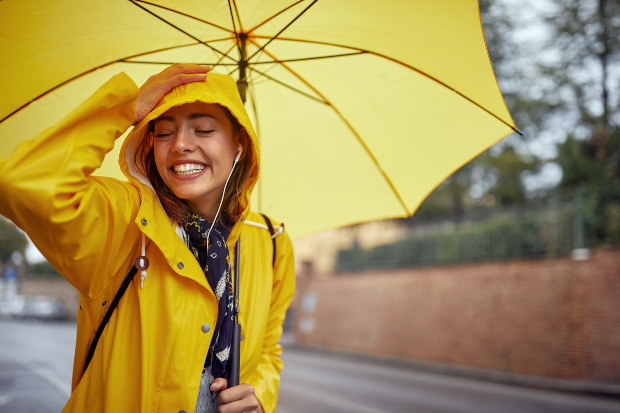 Eine Frau im gelben Raincoat geht bei Regenwetter spazieren