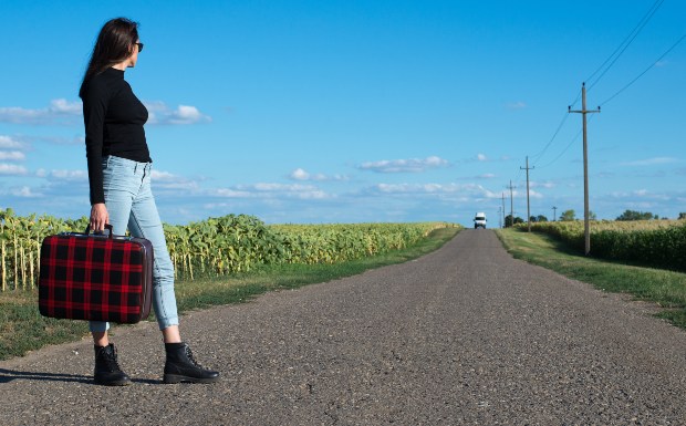 Junge stylische Frau am Straßenrand mit cropped Jeans trägt einen Koffer