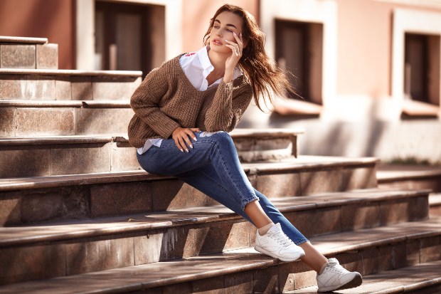 Junge Frau sitzt auf einer Treppe, modisches Outfit mit cropped Jeans