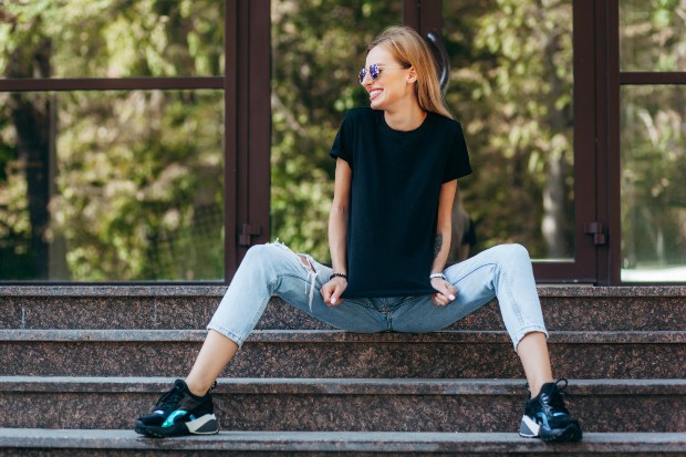 Junge Frau, cropped Jeans, T-Shirt und Sneakers sitzt auf einer Trepppe