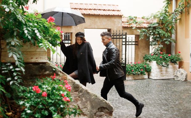 Junges Paar mit Regenschirm flüchtet vor dem Regen in ein Haus