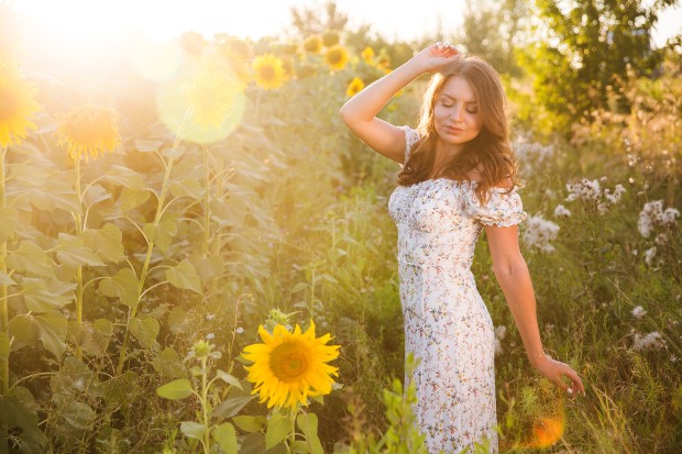 Junge Frau in Sommerkleid mit Rüschen im Sonnenblumenfeld