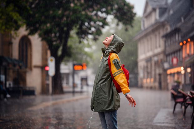 Junge Frau in einer Innenstadt freut sich über den Regen - Regenmode